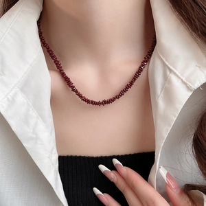 Detailed macro view of an irregular burgundy stone beaded necklace on a white shirt