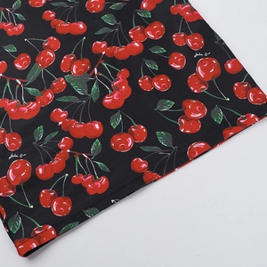 Detailed view of cherry print fabric with red cherries and green leaves on black background