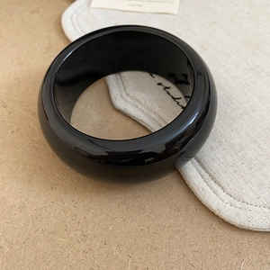 Close-up of minimalist black resin bangle with high-gloss finish on natural linen fabric