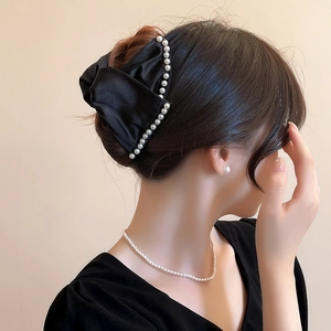 Detailed view of an elegant black satin bow hair claw clip with white pearl trim decoration