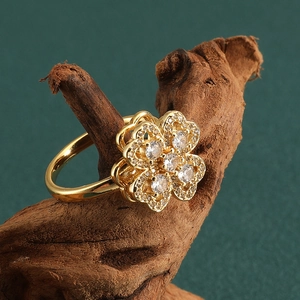 Golden rotating clover ring with white zircon stones on a natural wood surface