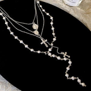 Detail of layered Y2K cross pearl necklaces with religious medals on black velvet