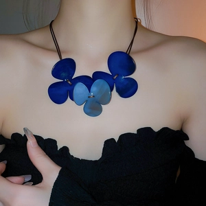 Detail of oversized blue triple-petal flower pendant necklace on a model's neck