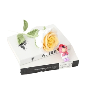 Hand-knitted white and yellow rose flower with a cute pink resin doll on books
