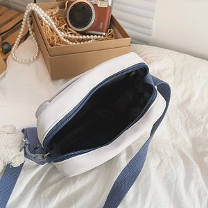 Détail du sac bandoulière en toile blanche avec intérieur bleu marine et chaîne de perles