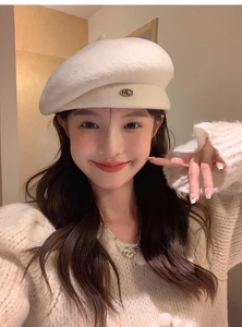 Detailed view of off-white wool beret featuring a metallic oval ML letter logo accent