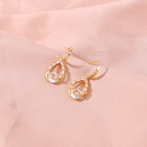 Detailed view of teardrop gold earrings with round white zircon on pink silk
