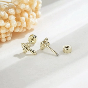 Golden fleur-de-lis cross screw-back earrings on a textured stone background