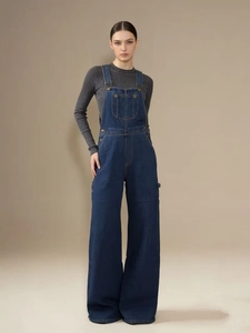 Détail d'une salopette en jean bleu foncé avec boucles métalliques et coupe large