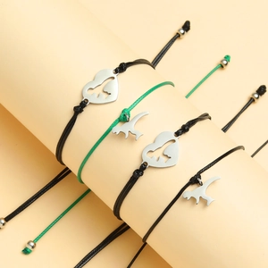 Detail of woven dinosaur bracelets in black and green with silver heart charms