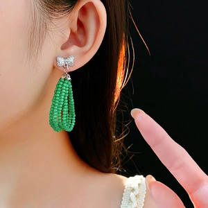 Detail of silver bow earrings with elegant green beaded tassels on model with black background