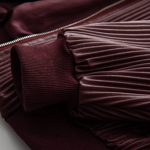 Macro shot of burgundy faux leather sleeve with pleated texture and ribbed knit cuffs