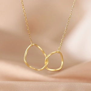 Macro view of gold plated double interlocking geometric rings on a beige silk fabric