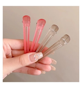 Hand holding four matte duckbill hair clips in red and taupe colors for hair styling