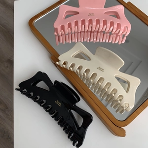 Détail de grandes pinces à cheveux en acétate noir, beige et rose avec lettrage doré