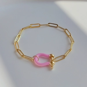 Detailed view of golden paperclip chain bracelet featuring a pink enamel U-shaped horseshoe clasp