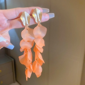 Macro detail of acrylic petal tassel earrings with gold leaf studs in orange finish