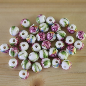 Macro shot of white ceramic beads with pink floral patterns on a light wooden background