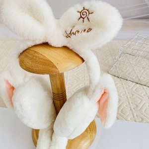 Close-up of plush rabbit ear muffs with soft white fur and pink inner lining details
