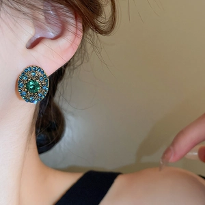 Detail of vintage oval earrings with green gemstone and blue crystals on a model