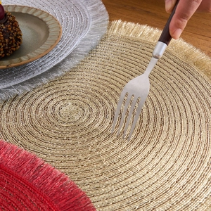 Macro detail of round woven placemats with fringe in gold, silver, and festive red colors