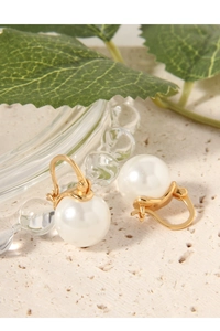 Macro shot of elegant white pearl earrings with gold clasp on a stone surface