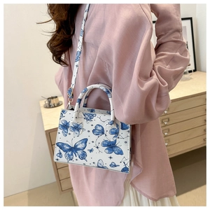 Dettaglio di una borsa bianca con motivi di farfalle blu e chiusura in metallo oro