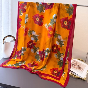 Detail of silk scarf with orange gold base and peony print draped on a table