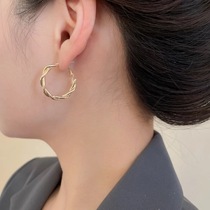 Close-up of elegant gold-tone twisted hoop earrings worn by a model in natural light