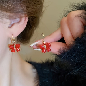 Gros plan d'élégantes boucles d'oreilles nœud rouge et or portées par un mannequin
