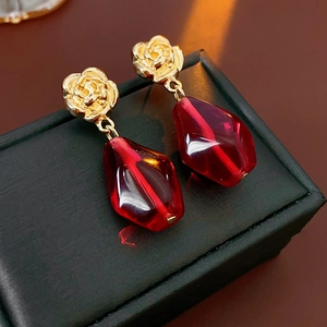 Close-up of golden rose earrings with red teardrop glass stones on a jewelry box