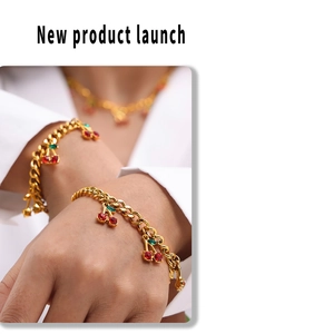 Close-up of gold chain bracelets with red cherry pendants and crystals on wrist