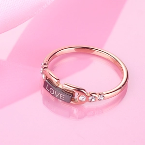 Rose gold titanium ring with love engraving and crystals on reflective pink surface