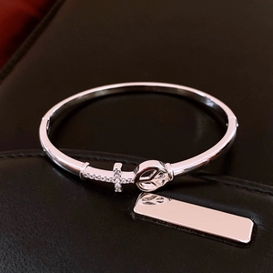 Detail shot of silver bangle with cross and peace symbols on black leather texture