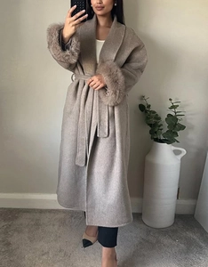 Détail d'un manteau long beige avec poignets en fausse fourrure et ceinture à la taille