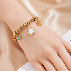 Golden beaded chain bracelet with turquoise stone and flower charms on silk background