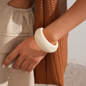 Detail of a chunky cream resin bangle on wrist with natural linen background texture