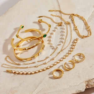 Vue à plat de bracelets et bagues dorés avec pierres vertes et perles sur pierre