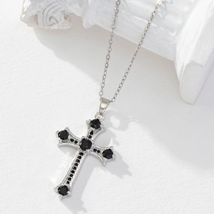 Elegant silver cross necklace with black round gemstone on white marble background