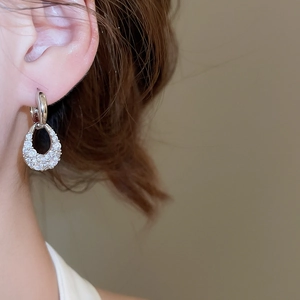Close-up of sparkling zircon teardrop earrings in C-shape design worn by a model
