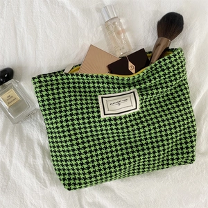 Detail of green houndstooth makeup bag with zipper closure and woven text label