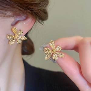 Detail of gold floral stud earrings with textured petals and three-dimensional metallic finish