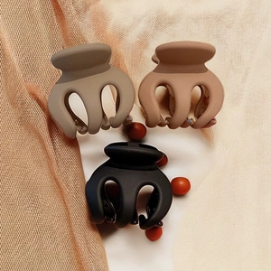 Three matte pumpkin claw clips in brown, beige, and black on a soft textured fabric