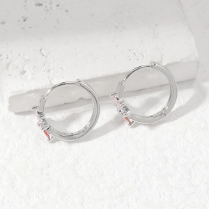 Silver huggie earrings with pink, purple and red zircon stones on a white stone background