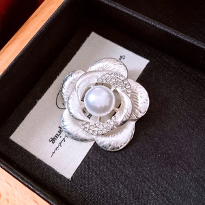 Macro detail of silver camellia flower brooch with pearl center and diamond accents