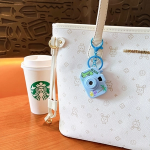 Creative blue dinosaur projection camera keychain with LED light hanging on a white bag.