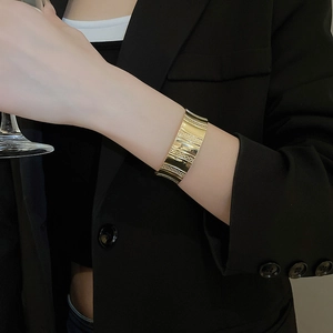 Close-up of polished wide gold textured cuff bracelet worn with a sleek black blazer