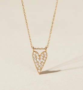 Macro detail of a heart-shaped gold necklace pendant with micro-pave white zircon stones