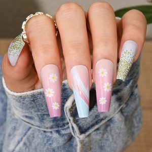 Close-up of long ballerina press-on nails with daisy patterns and gold glitter accents