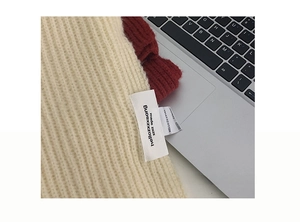 Close-up of thick knit scarf texture showing beige and red stitching with a woven label